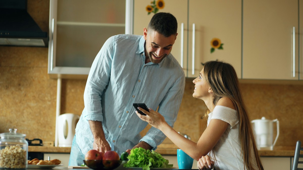 Couple in a bright kitchen looking at a phone, exploring free web tools for teachers.