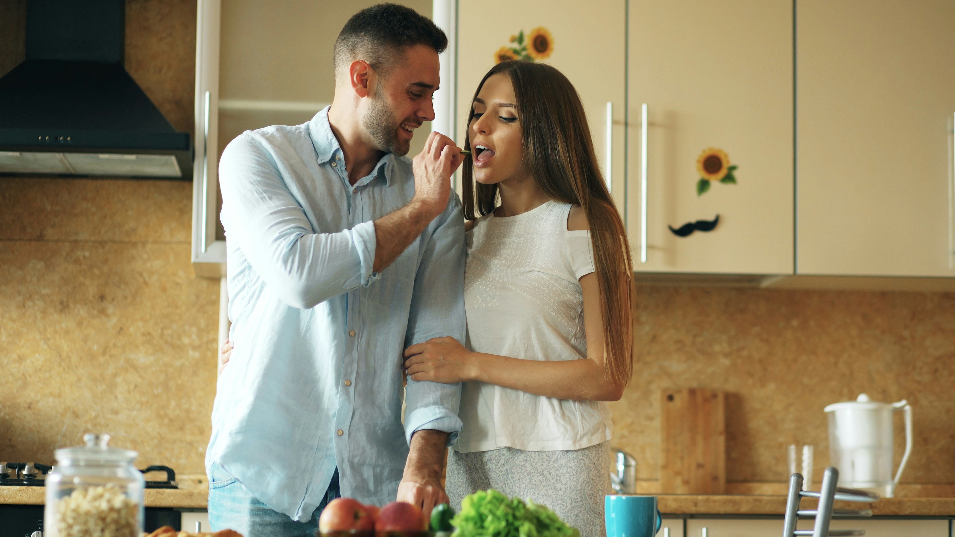 Happy young couple in the kitchen. Handsome man meet and feed his girlfriend early morning at home