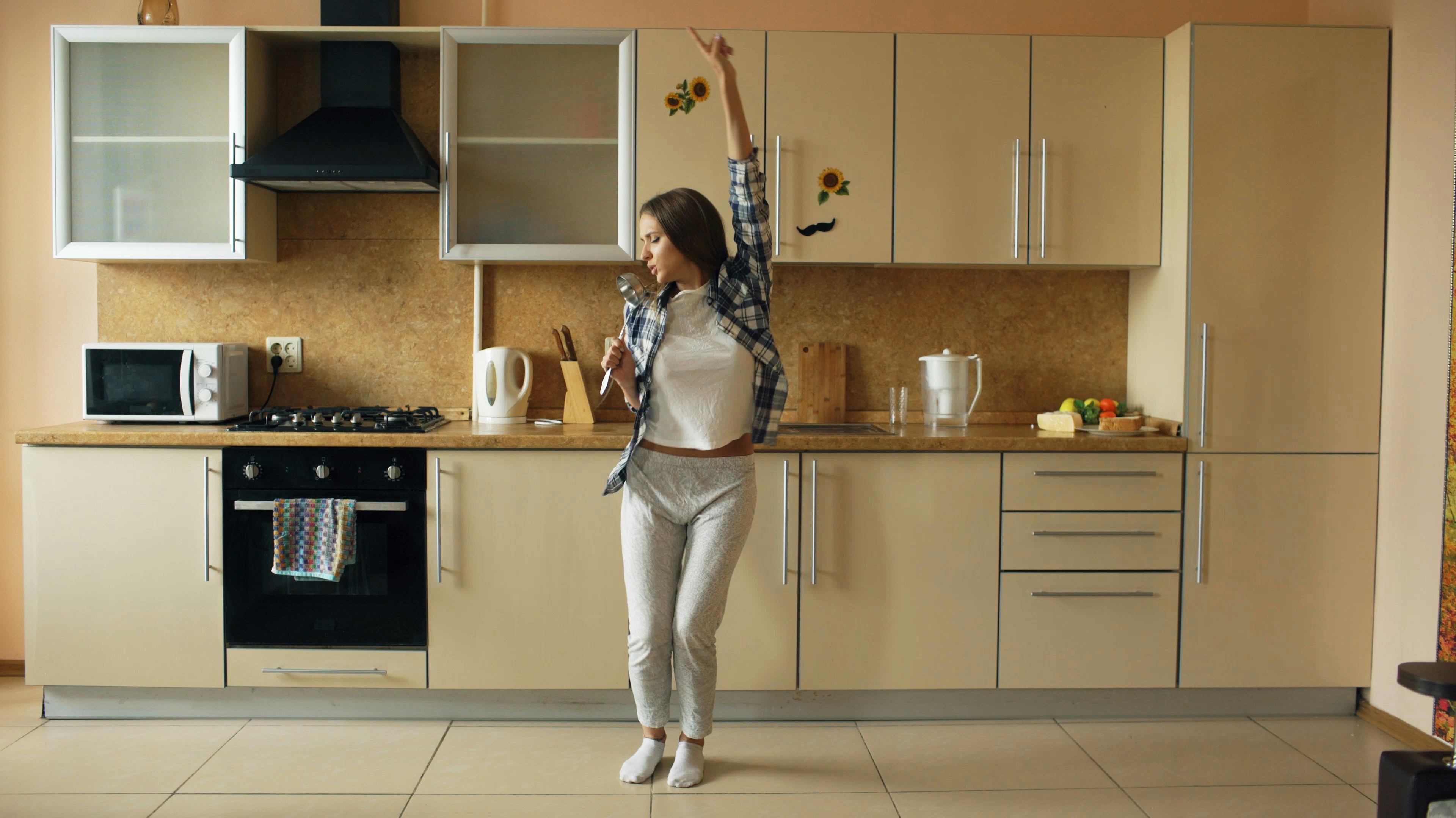 Young woman dancing and singing in a kitchen.