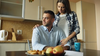 Woman comforts man at kitchen table with food.