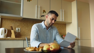 Man reading document at kitchen table with fruit and fruit