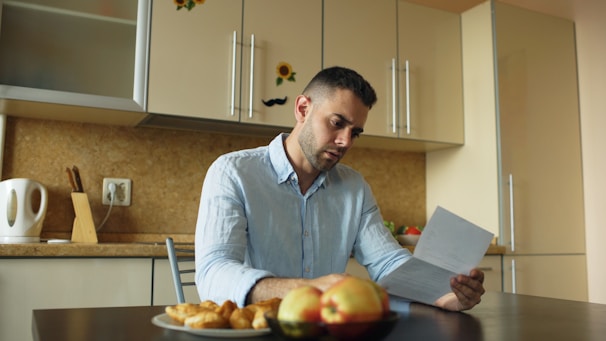Man reading document at kitchen table with fruit and fruit