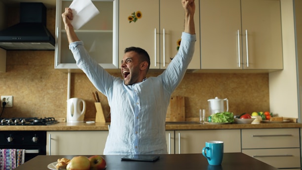 Man celebrating with arms raised in kitchen.