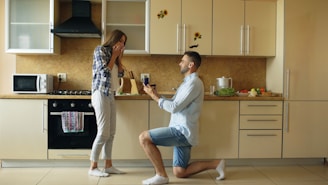 Man proposes to surprised woman in kitchen.