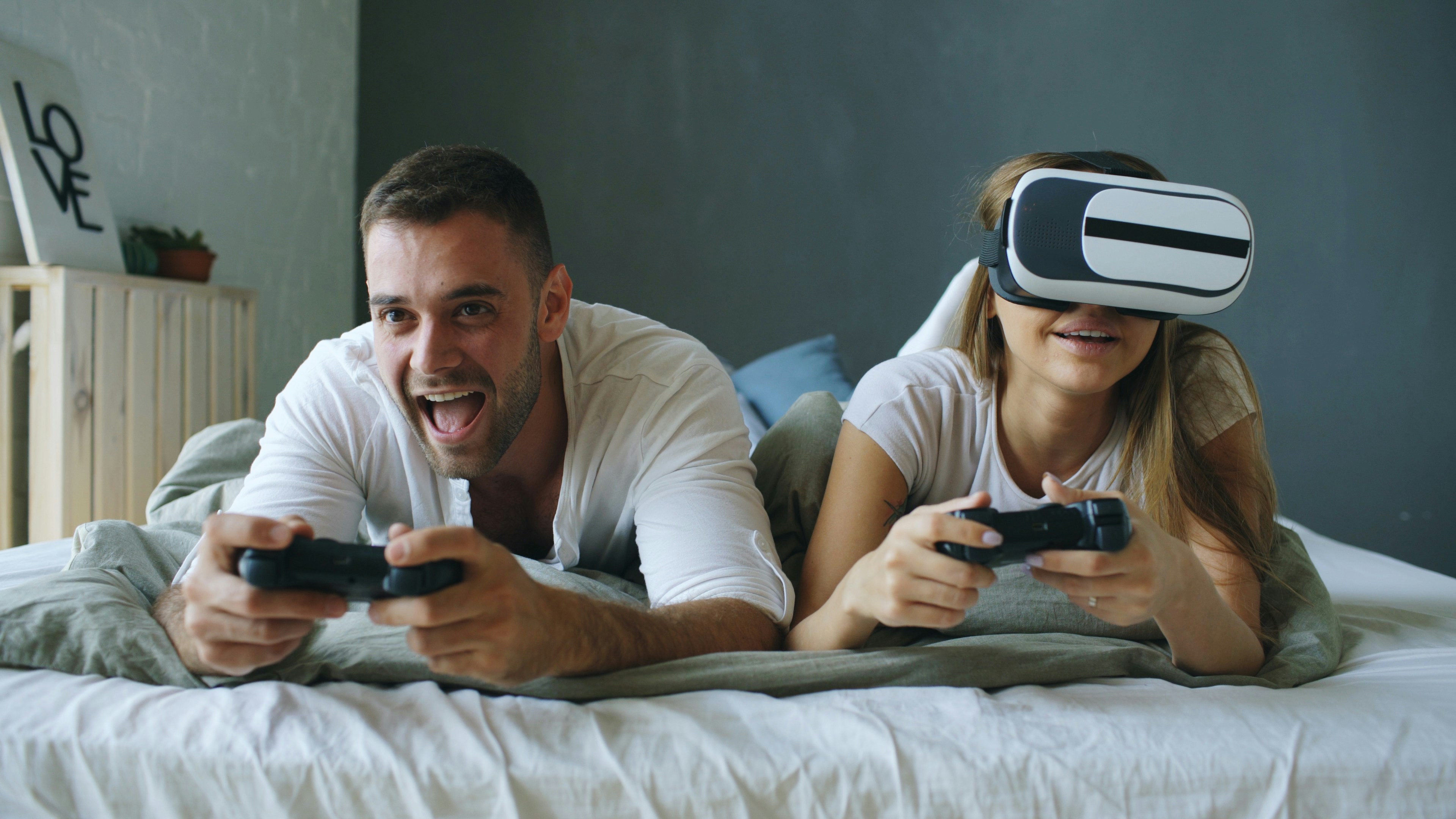 Couple playing video games with VR headset on bed