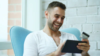 Man laughing while holding credit card and tablet.
