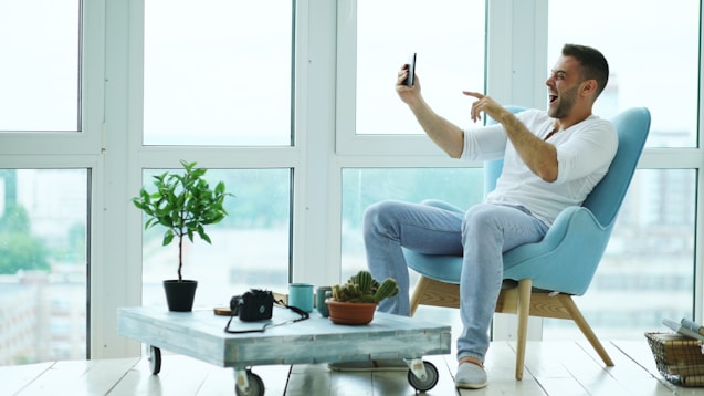 Man sitting in chair taking selfie with phone.