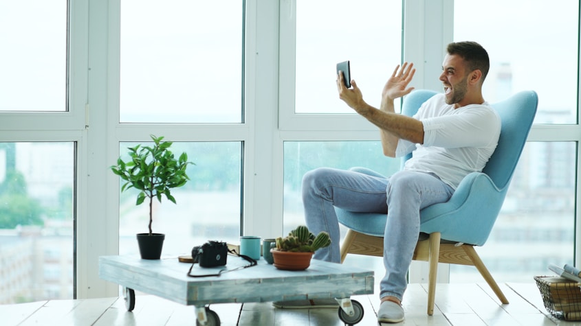 Man waving at phone while sitting in armchair.