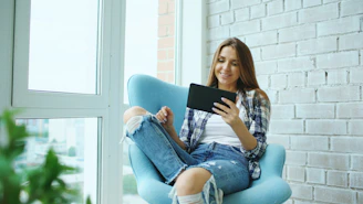 A young woman sits in a chair using a tablet.