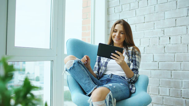 A young woman sits in a chair using a tablet.