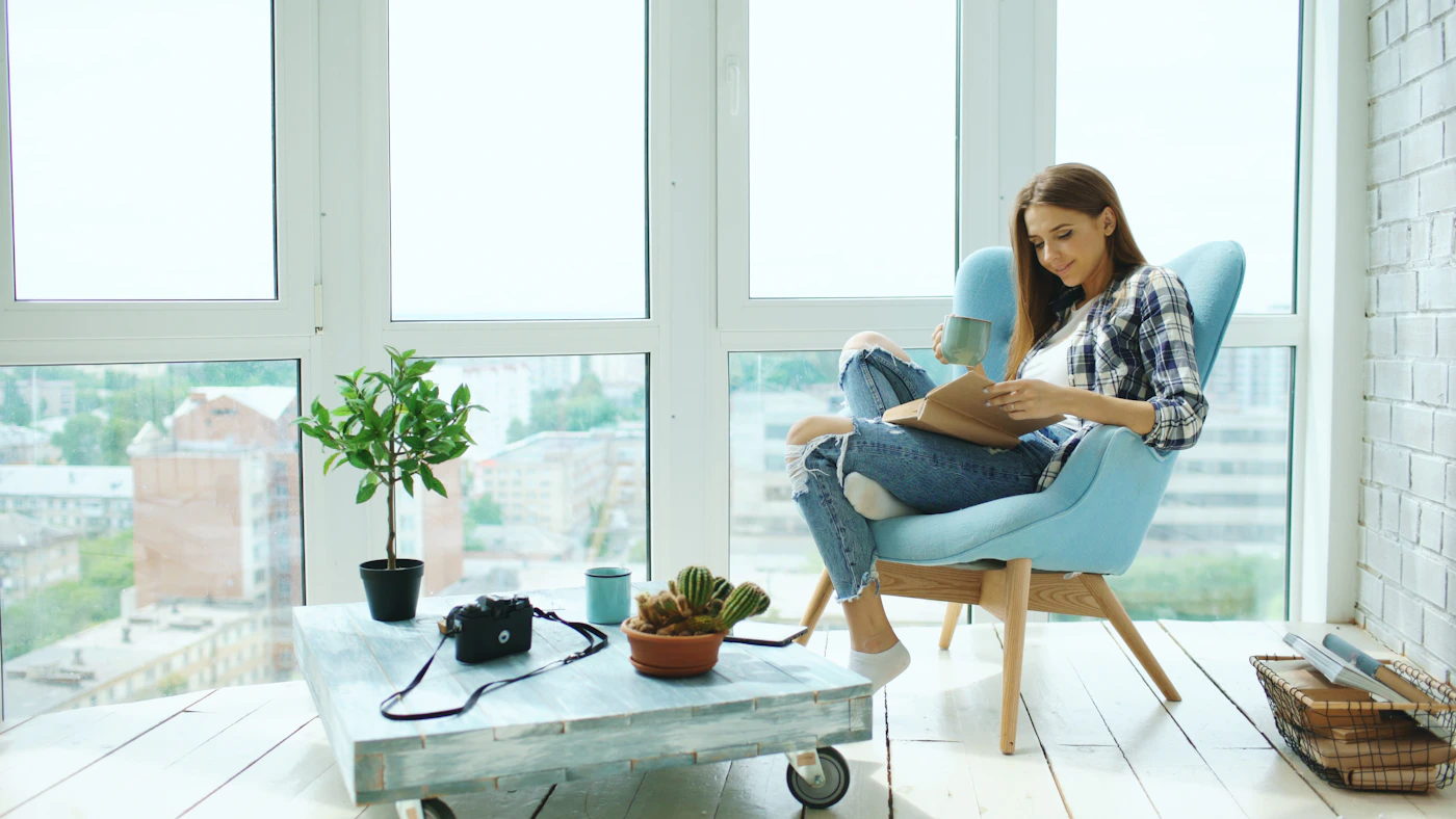 Woman reading alone by a window at home, representing rediscovering interests and quiet routines after a breakup