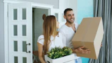 Couple carrying moving boxes and plant