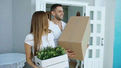 Couple carrying moving boxes into a new home