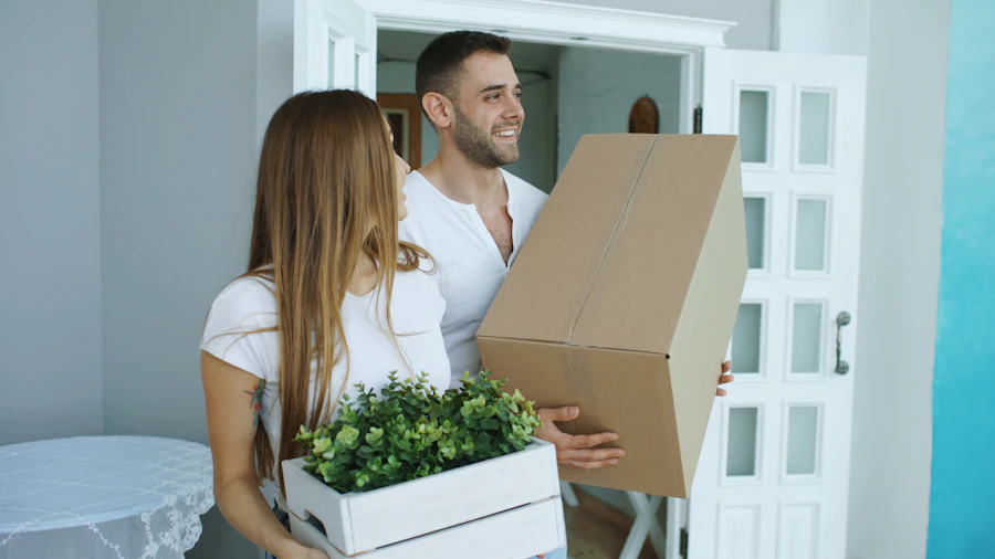 Couple carrying moving boxes and a planter through a doorway during a home cleanout