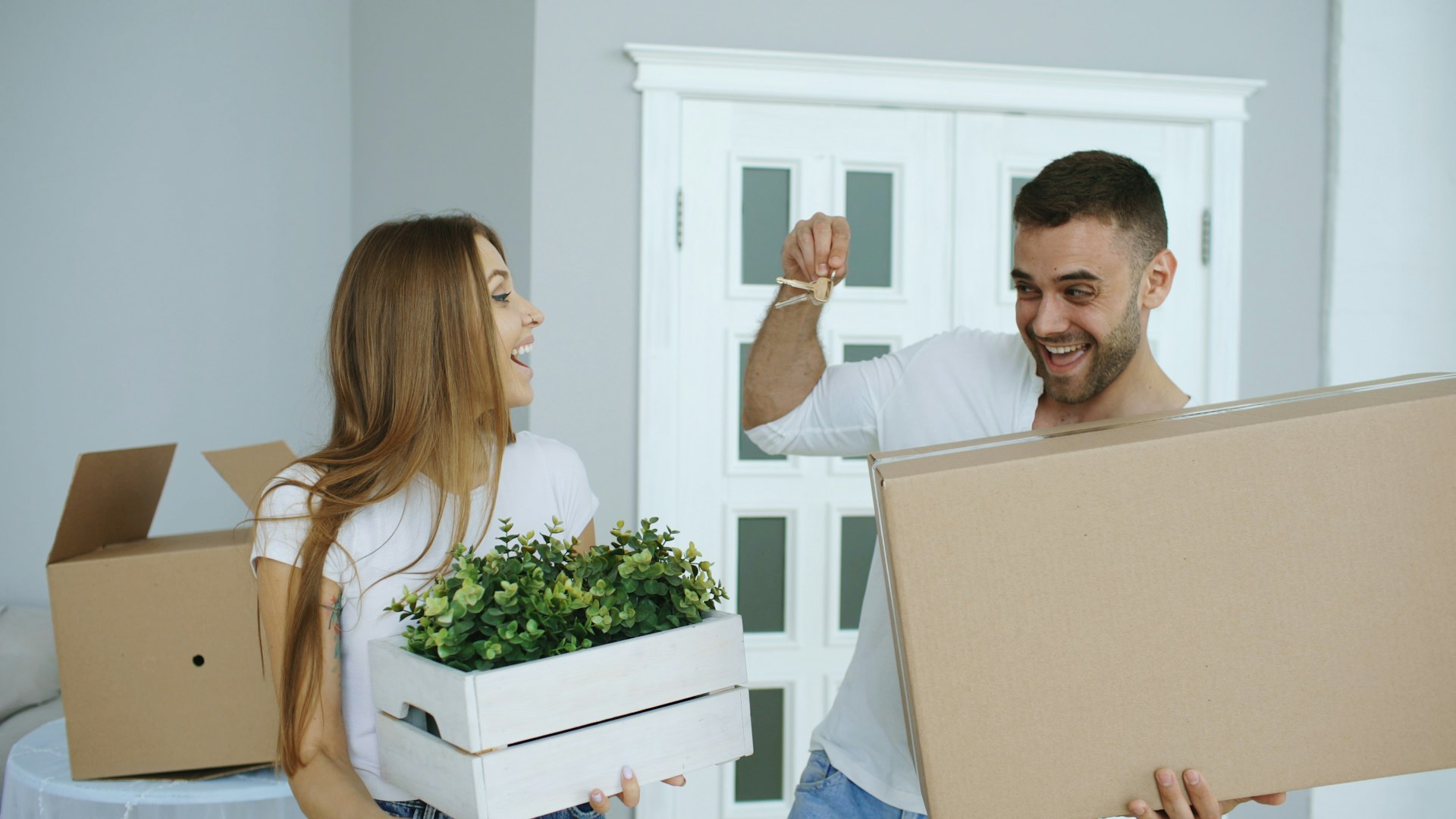 Couple holding up the keys to their new home among moving boxes