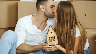 Couple kissing while holding a small wooden house.
