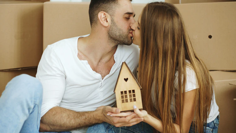Couple kissing while holding a small wooden house.