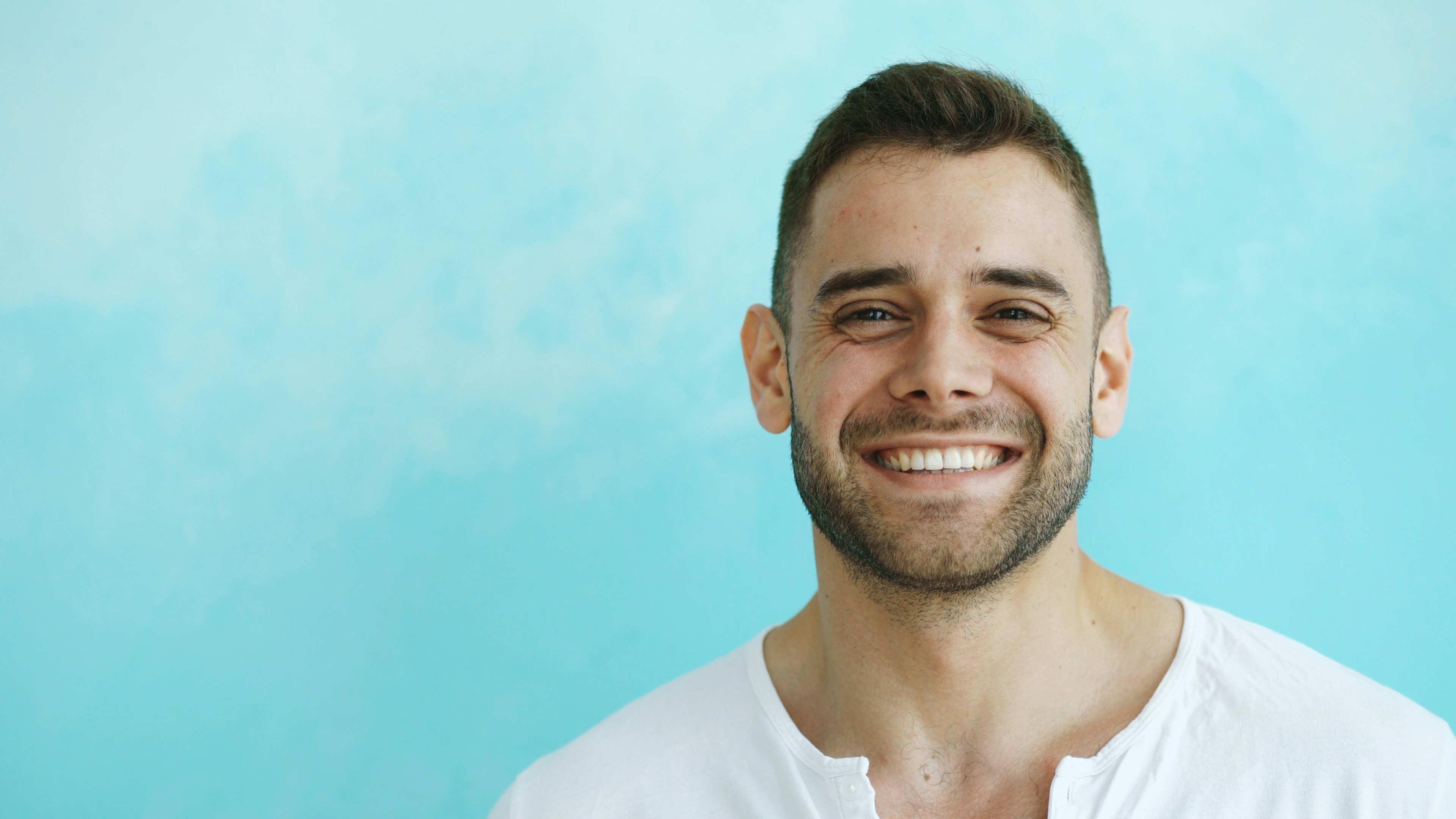Man in a white shirt smiling against a blue background
