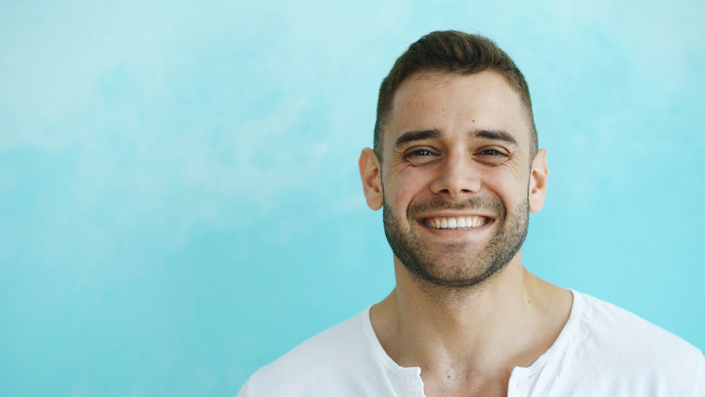 Smiling man with clear skin against a pale blue background