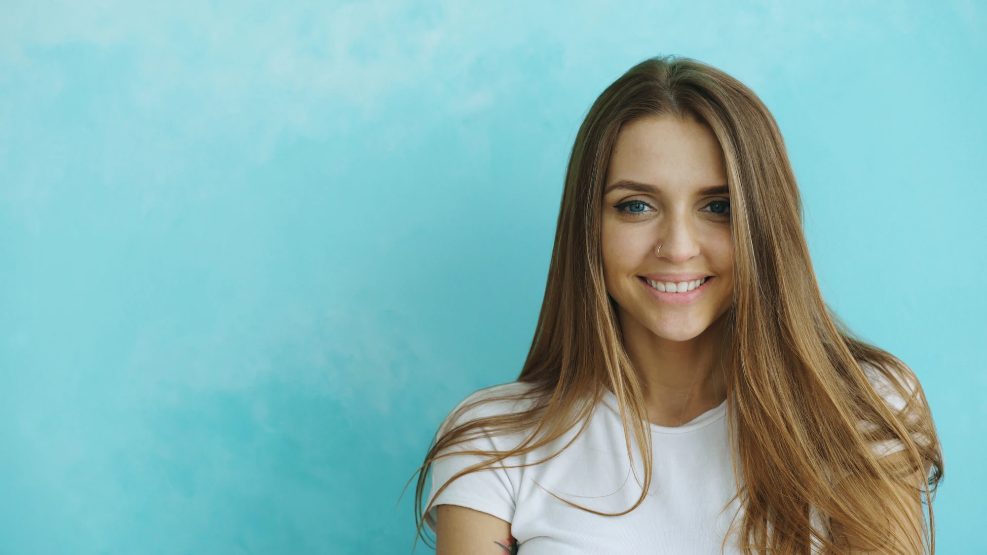 Smiling young woman with long brown hair against a sky blue wall