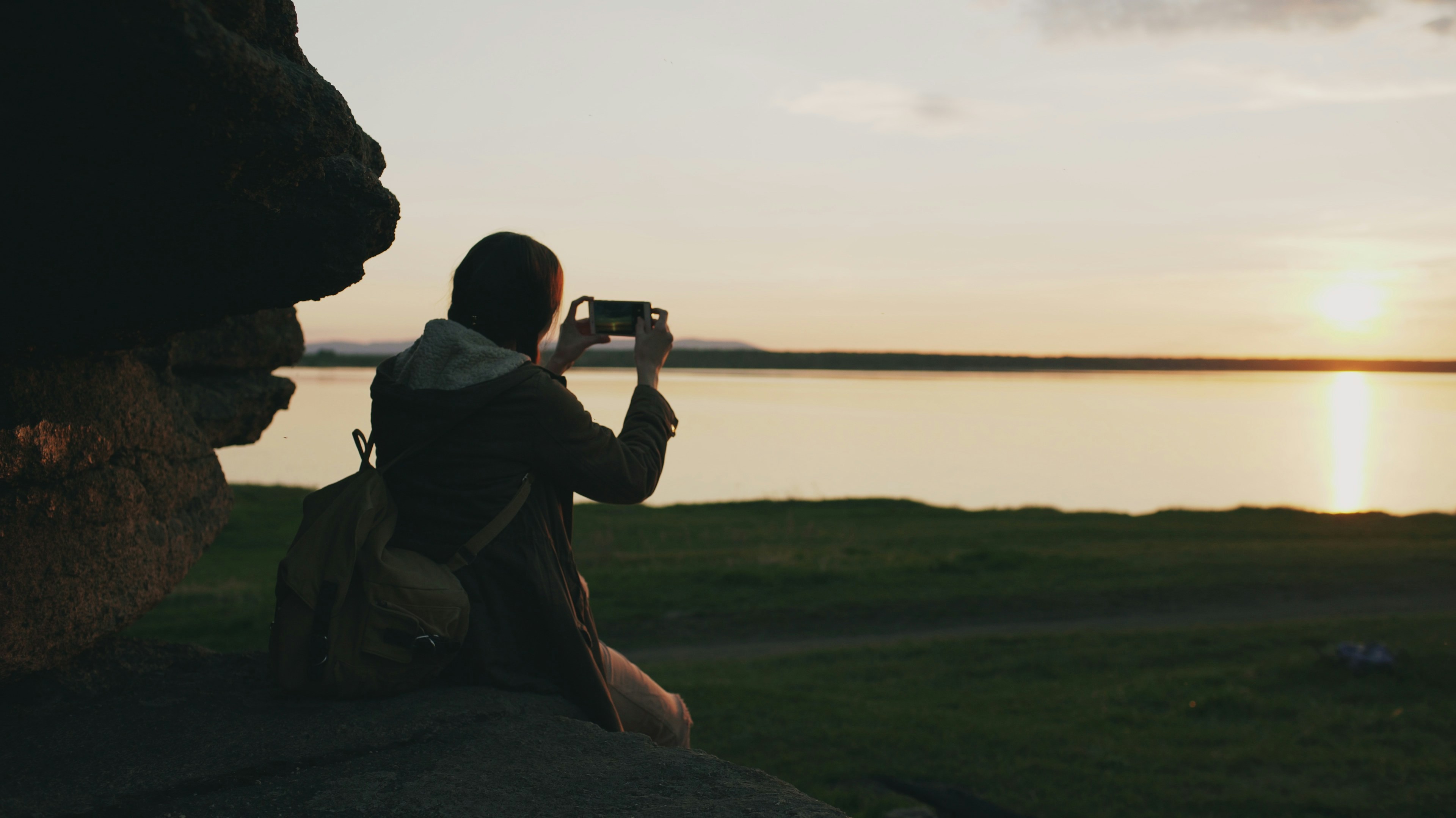 Fotógrafo usando smartphone como controle remoto para câmera em tripé no pôr do sol