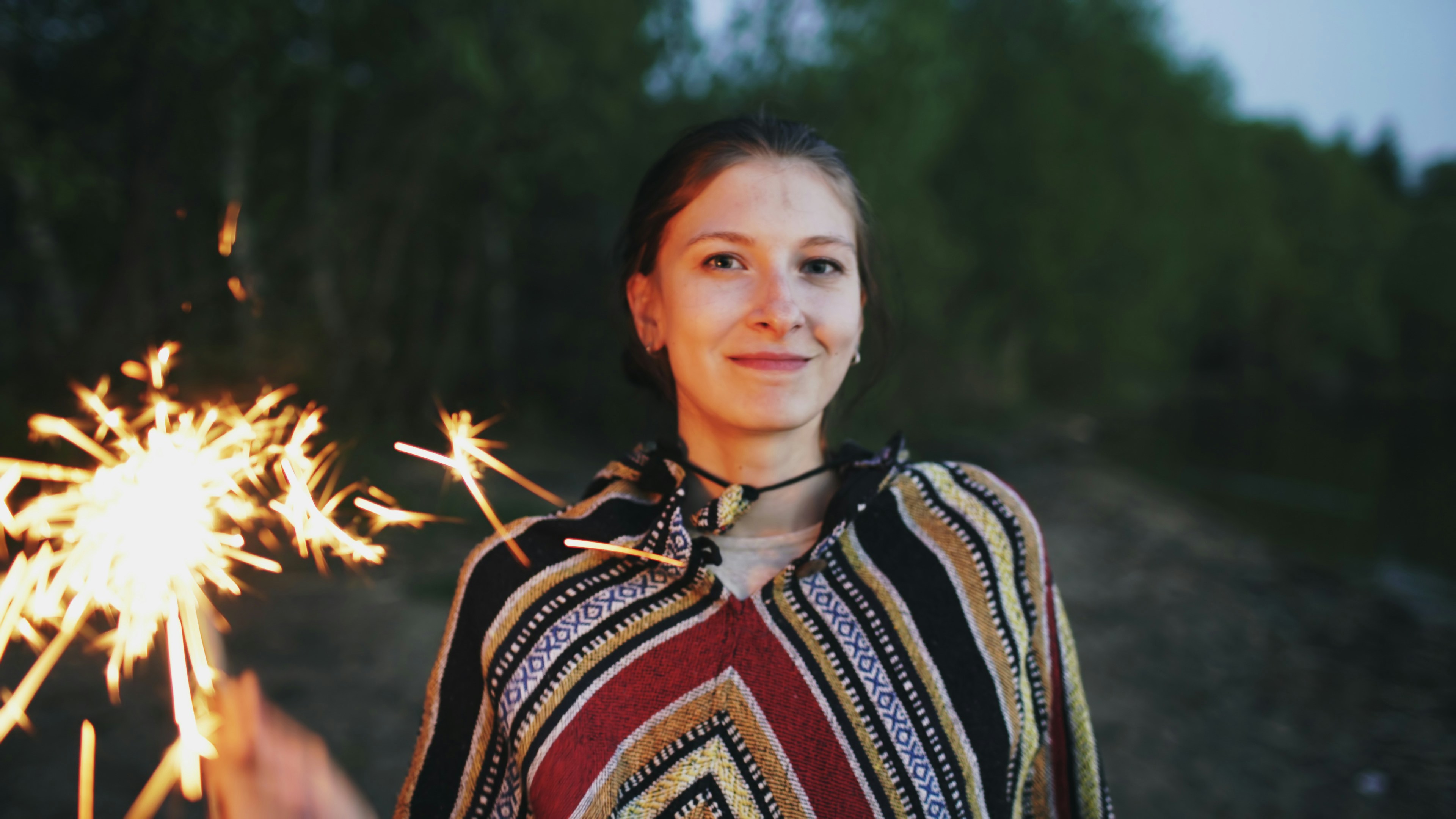 Young woman holding a sparkler at dusk
