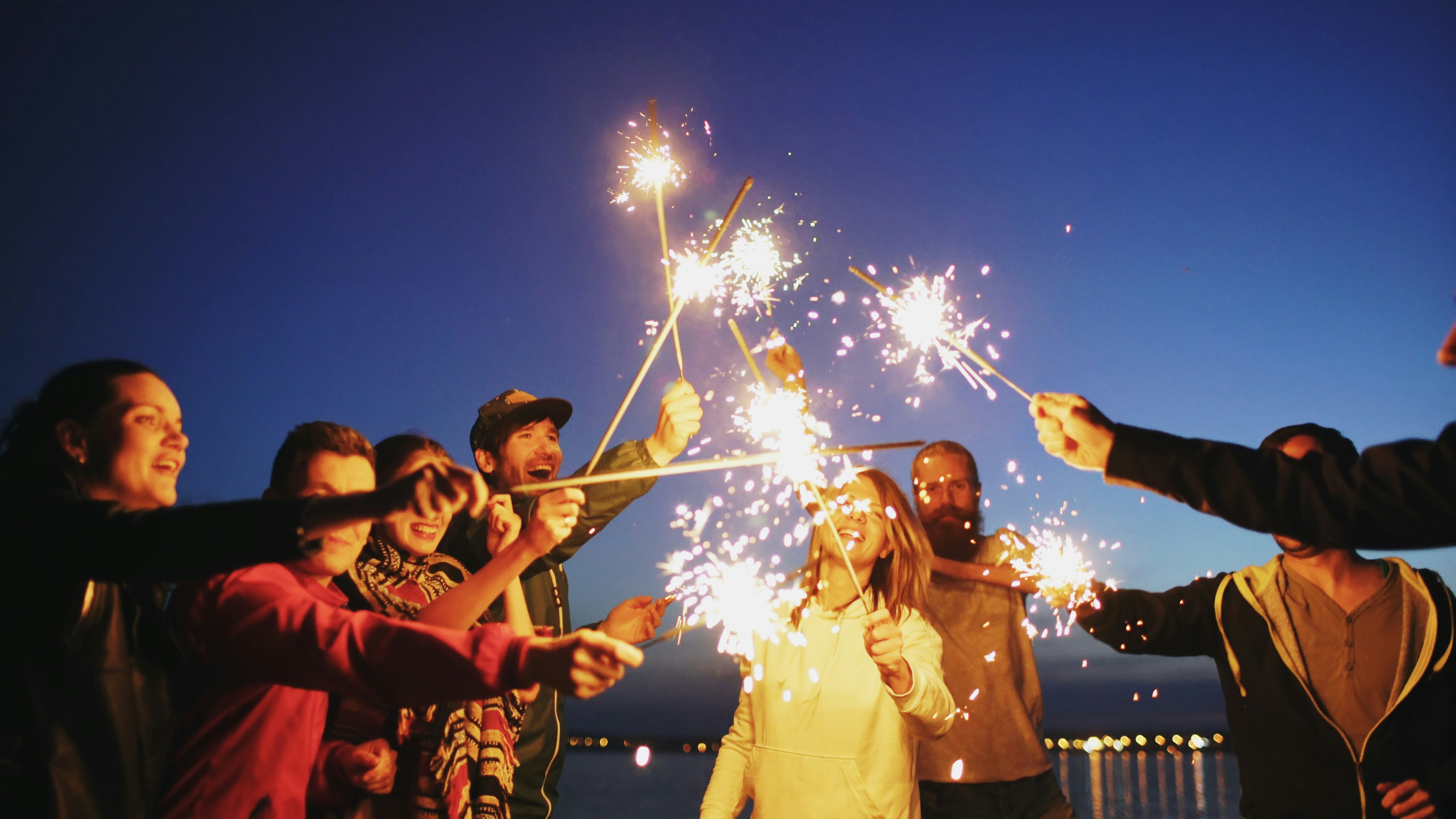 Group of young friends having a beach party. Friends dancing and celebrating with sparklers in the twilight sunset