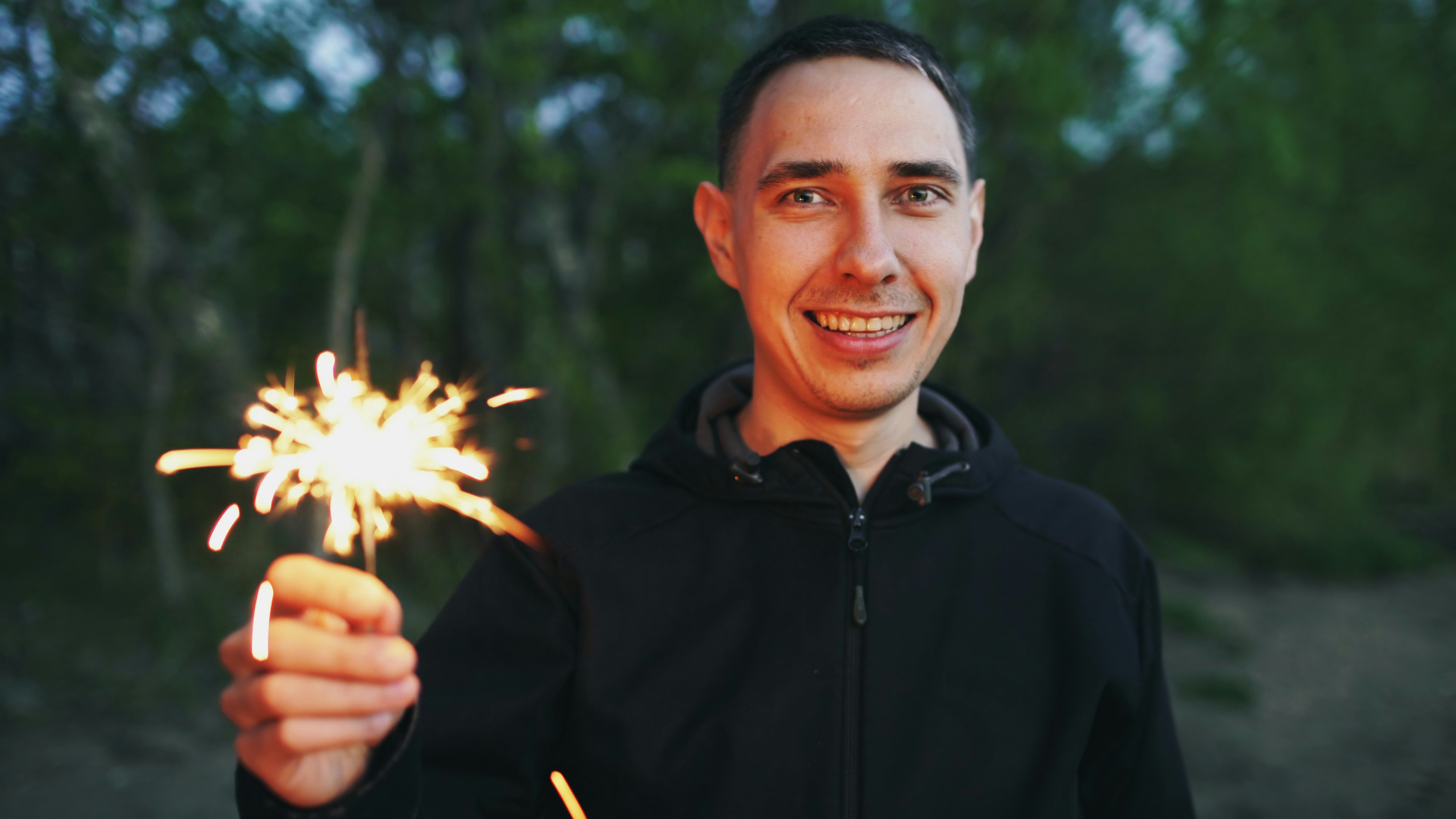 Man smiling and holding a sparkler outdoors