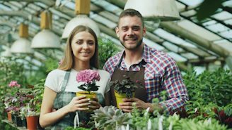 Couple holding potted plants in a greenhouse.