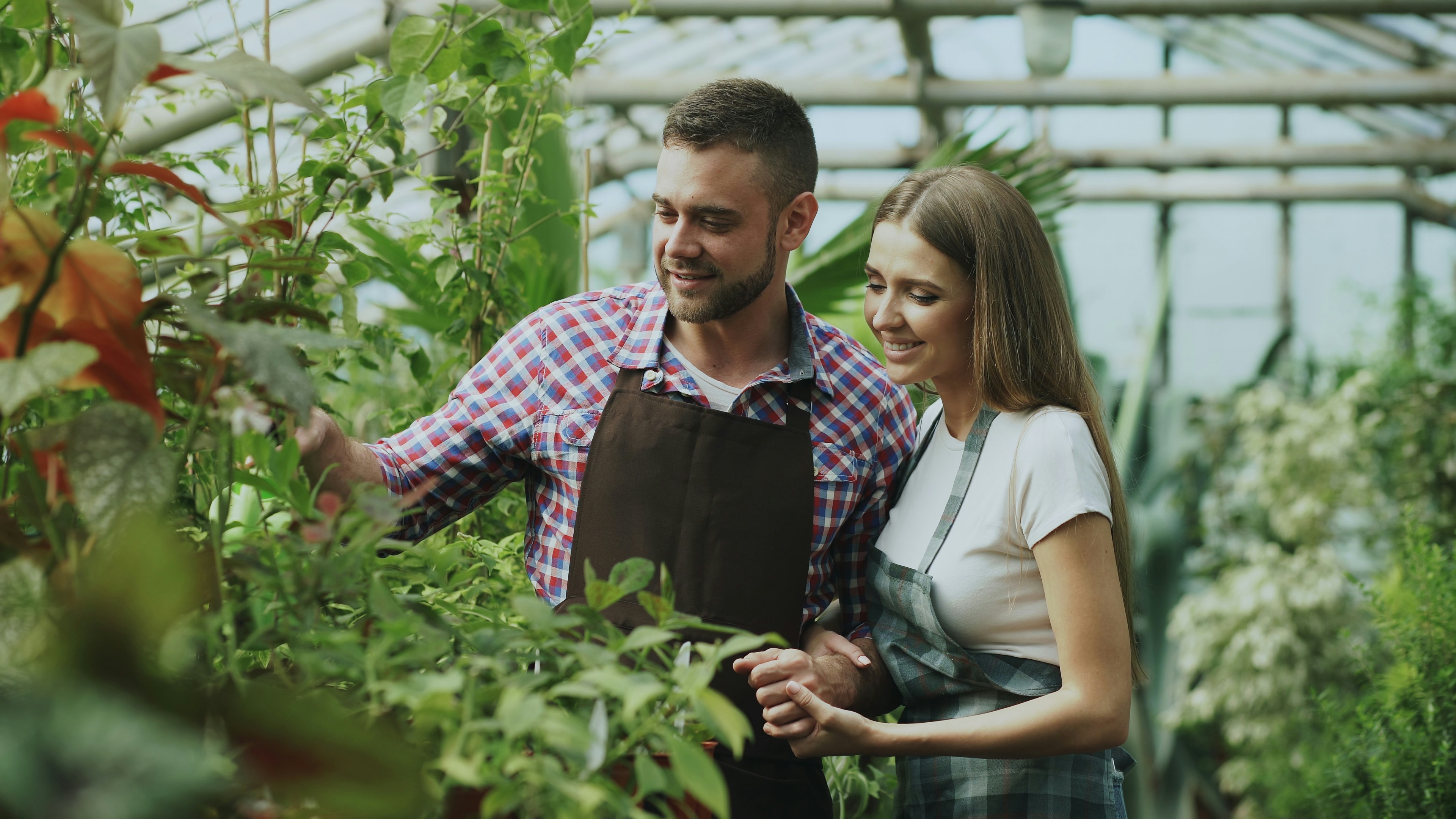 Man and woman tending plants in a greenhouse.