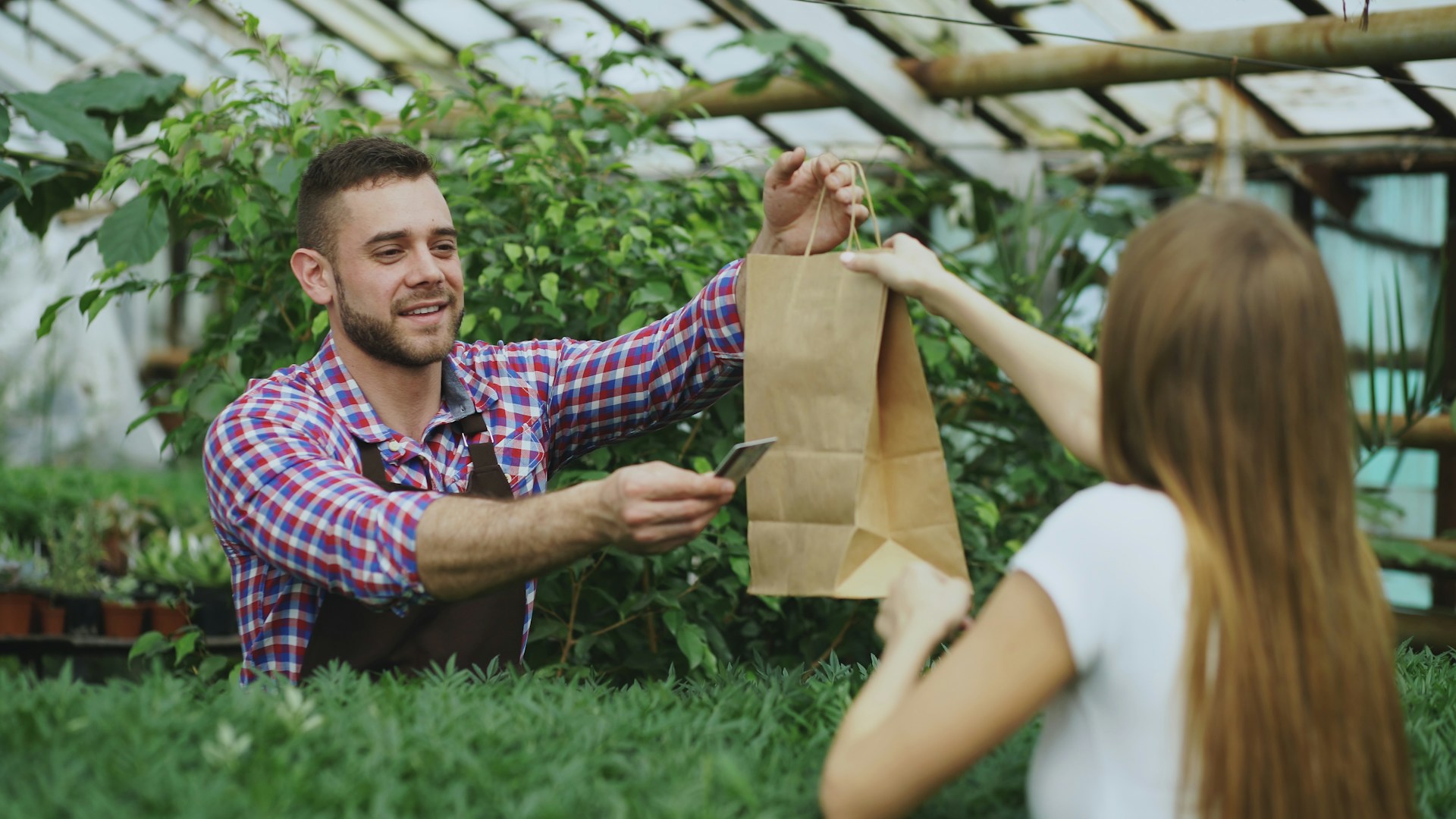 Man handing a paper bag to a woman in greenhouse