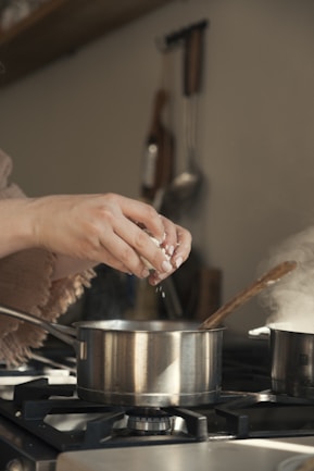 Hands adding ingredients to pot on stove