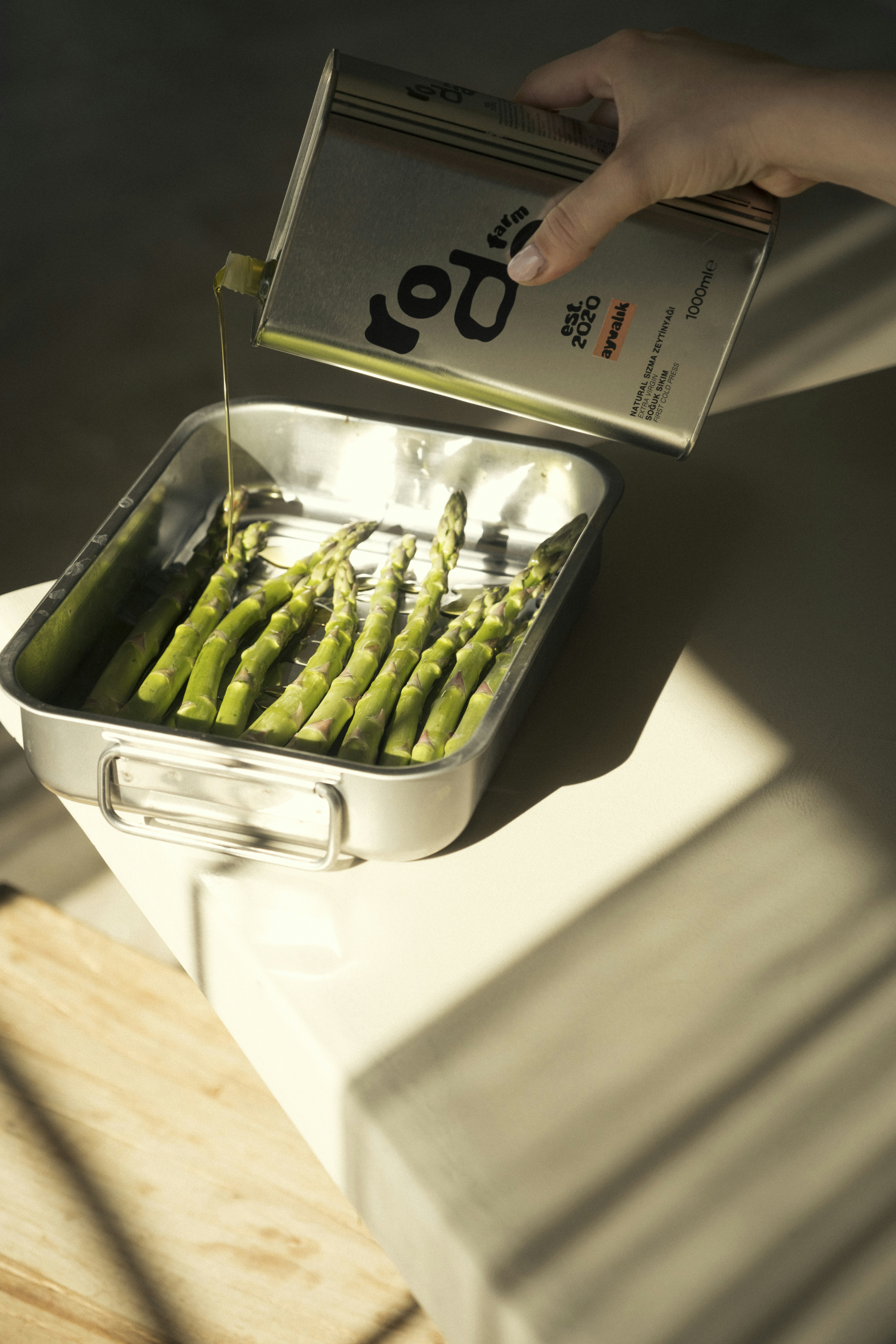 Pouring olive oil onto fresh asparagus in a pan.