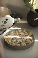 Olive oil being poured onto a plate of tortellini.