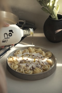 Olive oil being poured onto a plate of tortellini.