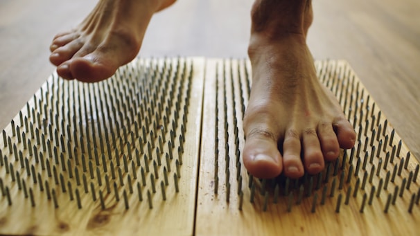 Feet stepping onto a wooden board with many nails.