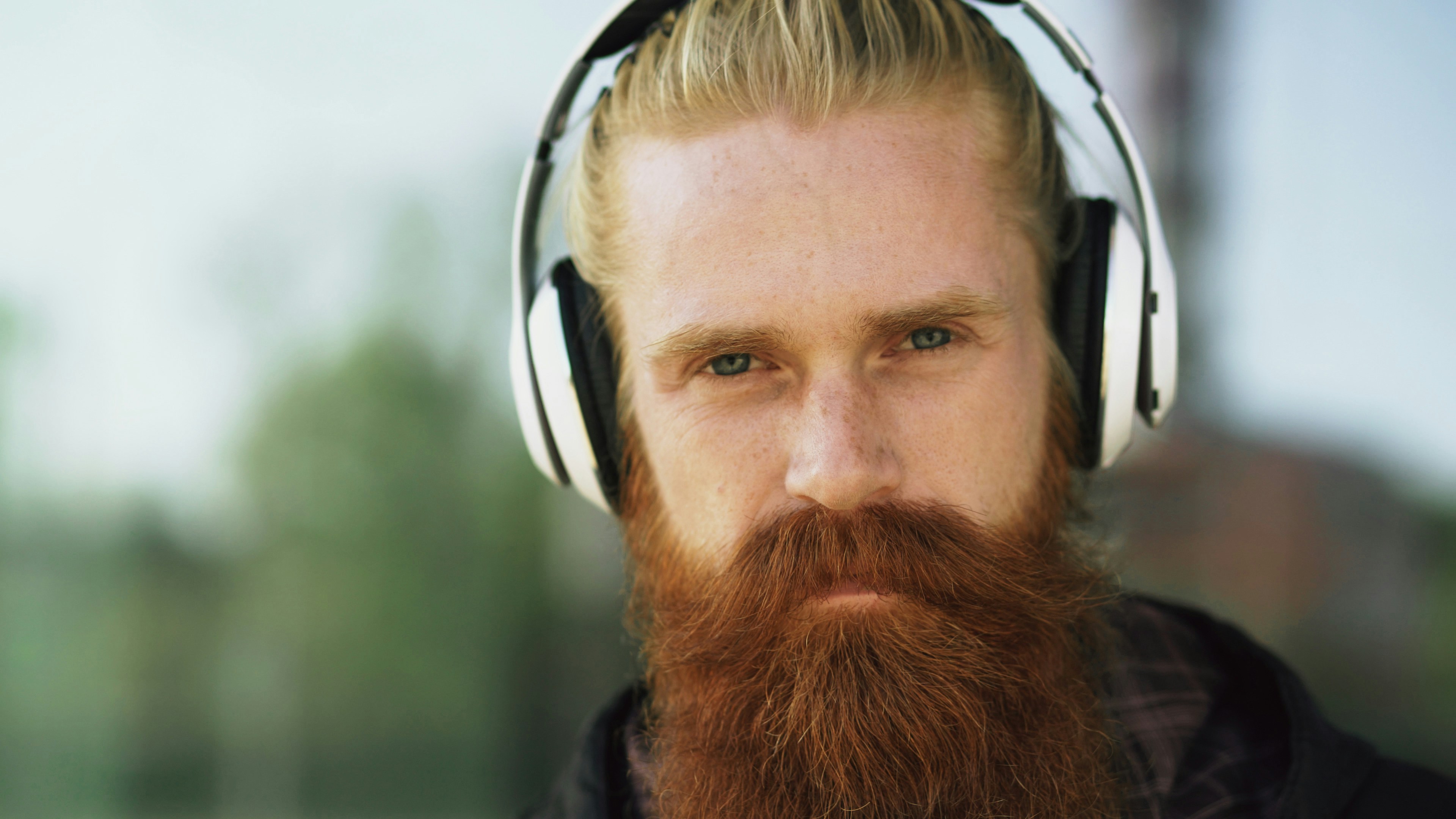 Closeup portrait of young bearded hipster man with headphones listen to music and smiling on city street