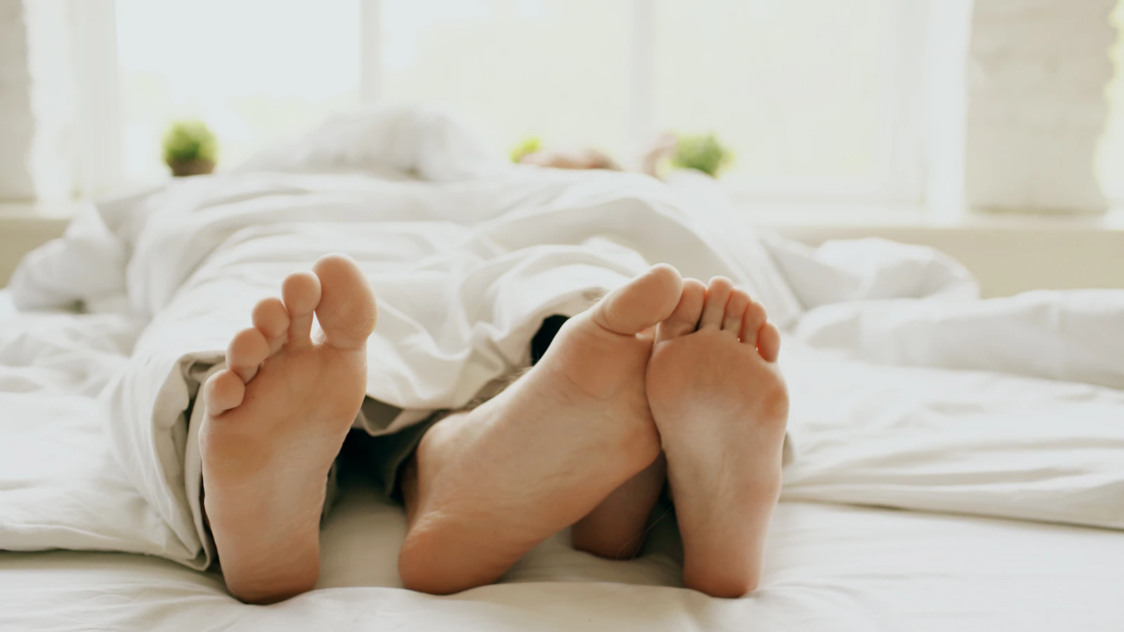 Couple's feet under a white duvet, intimate and quiet