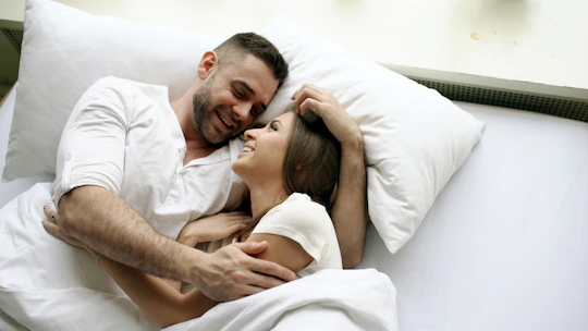 A couple embracing in bed, smiling at each other