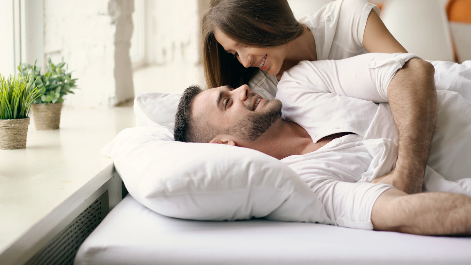 A couple lying together in bed in soft morning light, talking quietly