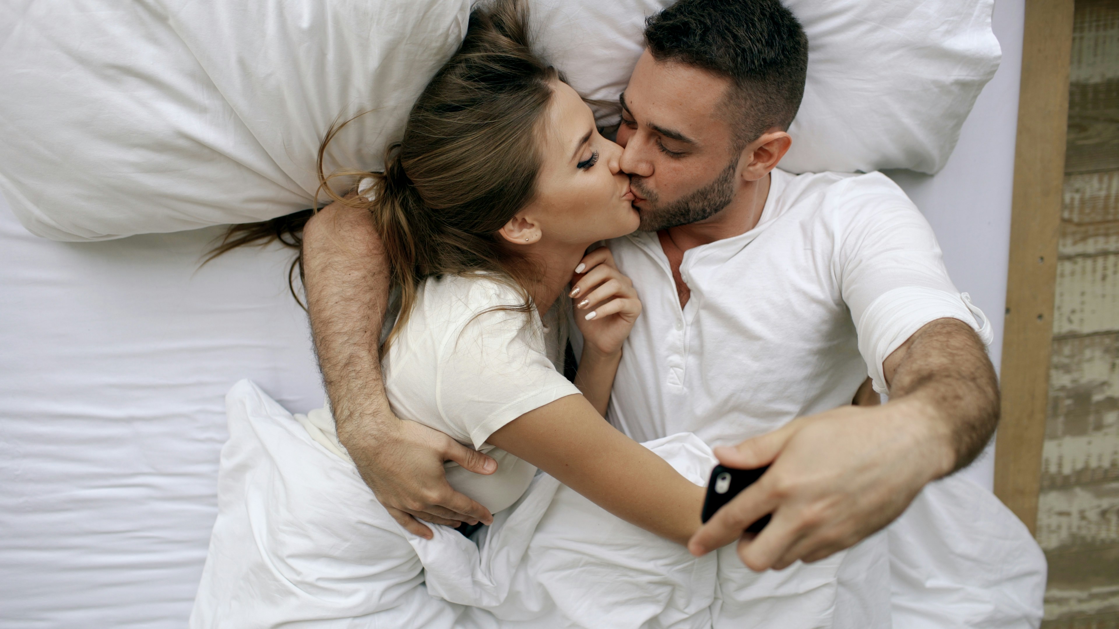 Couple kissing in bed while taking a selfie