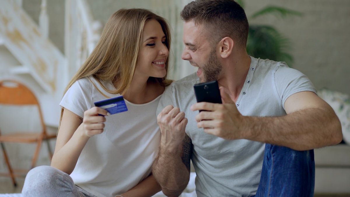 A couple smiling while completing an online purchase with a credit card and smartphone after watching a product video.
