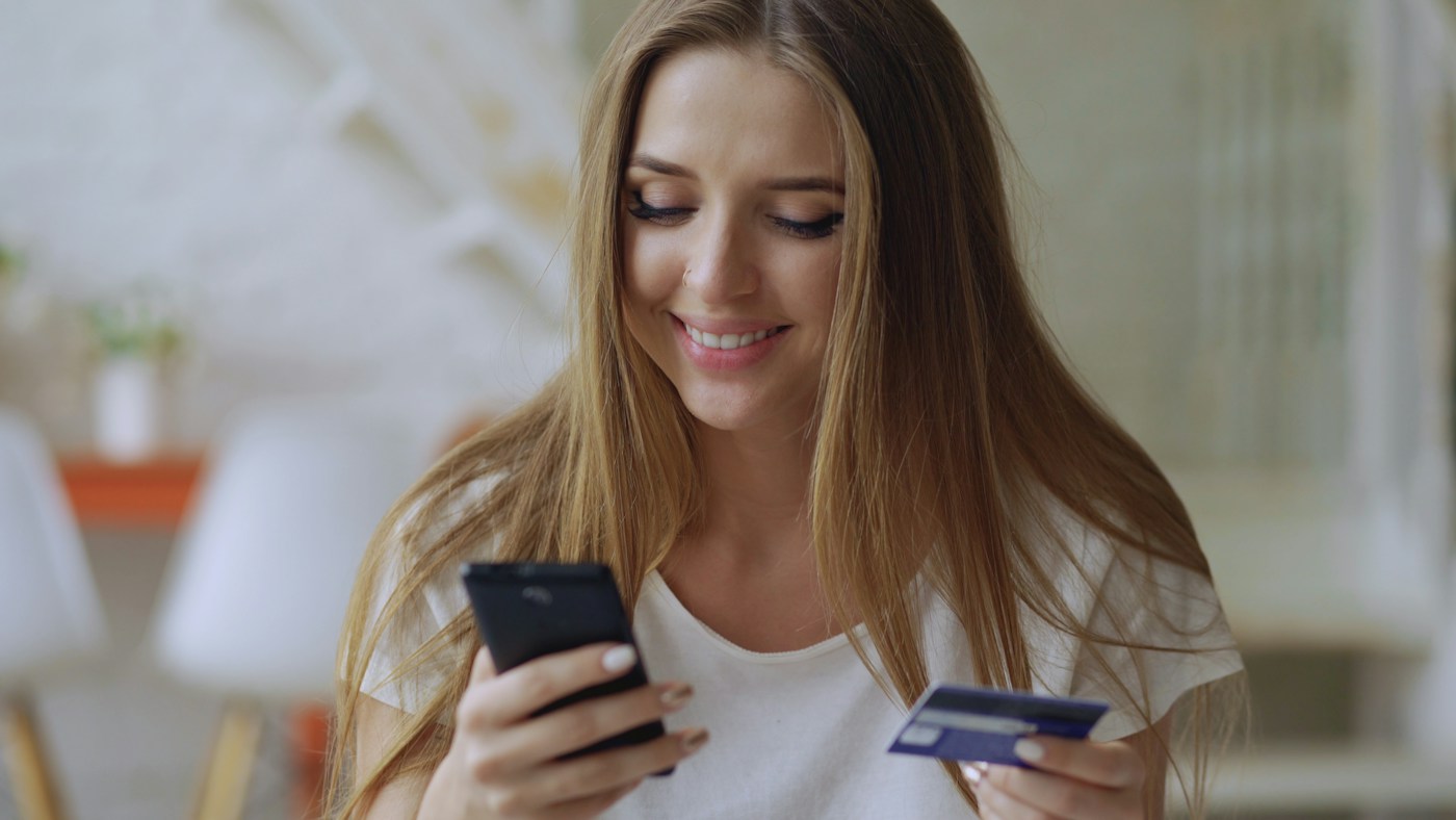 Mujer pagando desde el celular con una tarjeta en la mano