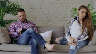 Couple sitting apart on a sofa, looking away