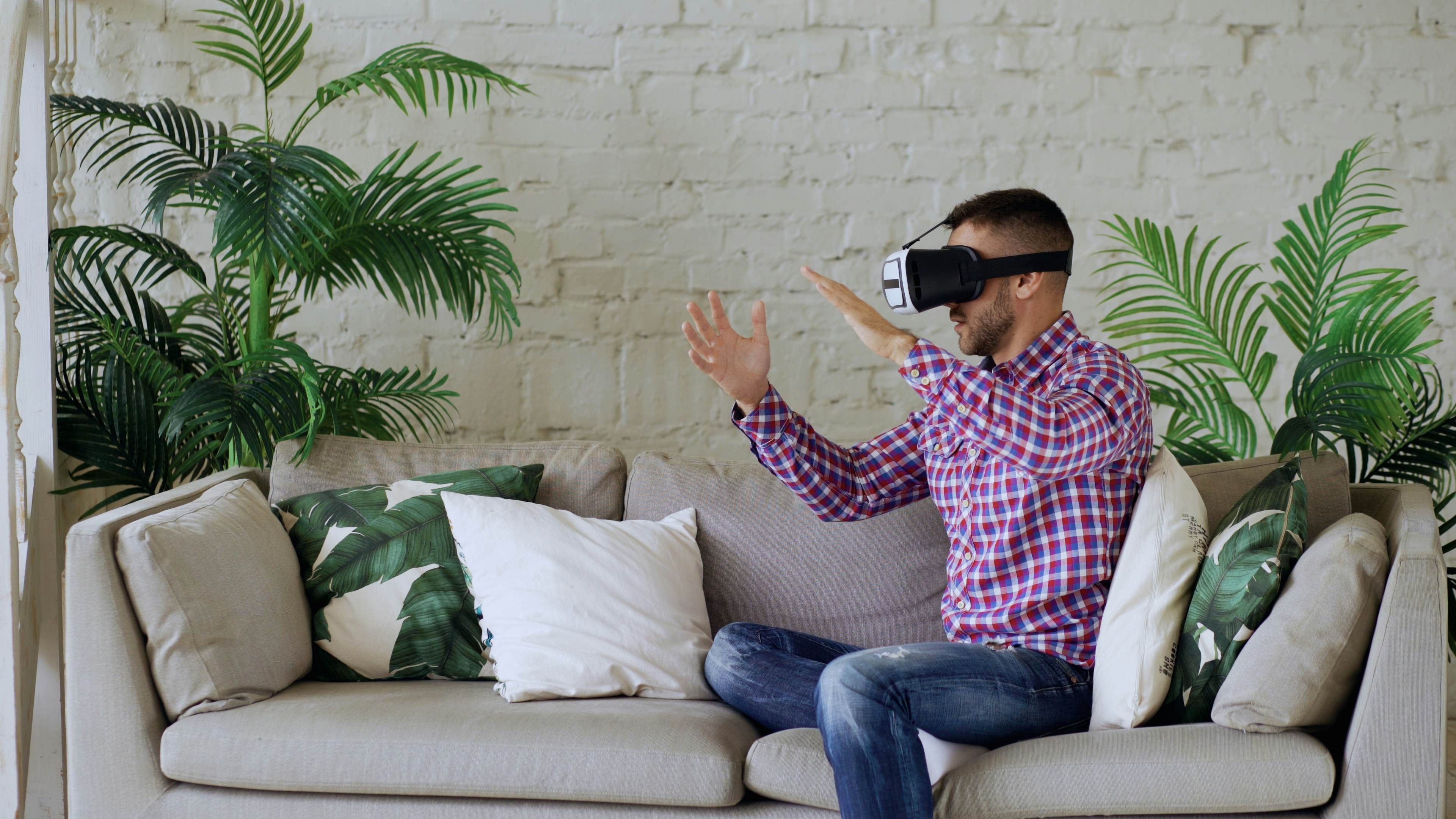 Man wearing vr headset sitting on couch, gesturing.