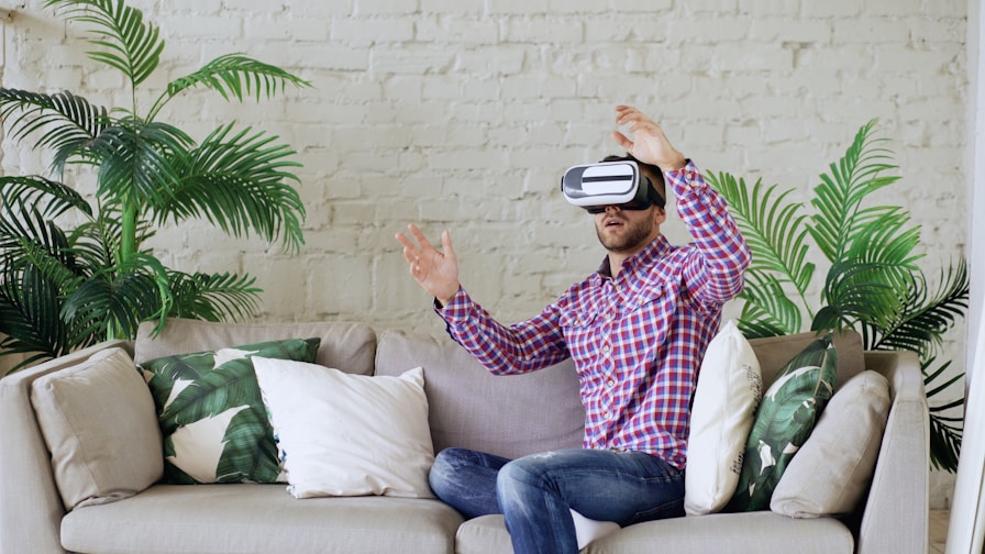 Man wearing vr headset sitting on couch, gesturing with hands.