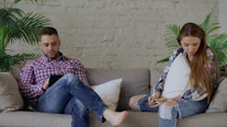 Couple sitting on sofa looking at phones