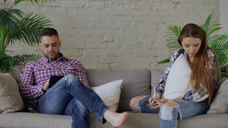 Couple sitting on sofa looking at phones