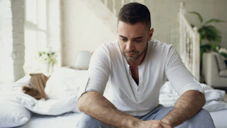 Man sitting on bed looking down thoughtfully