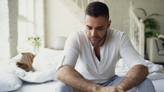 Man sitting on bed looking down thoughtfully.